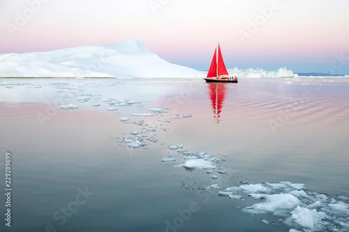 Obraz Mała czerwona żaglówka przelatująca wśród pływających gór lodowych w lodowcu Zatoki Disko podczas polarnego lata o północy. Ilulissat, Grenlandia.