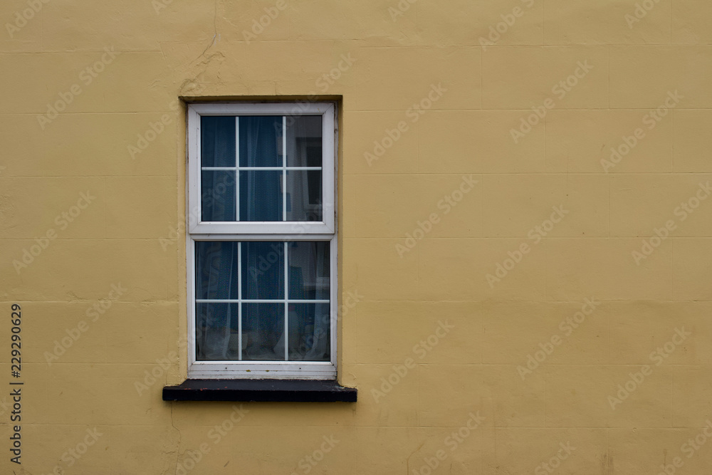 Close up view of a white window on a yellow or tan color European building cement wall background