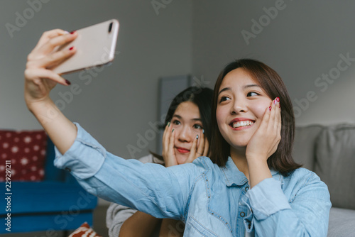 Two young female friends taking a picture of themselves with smartphone photo