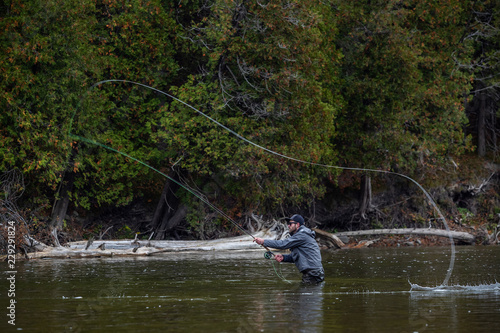 Man fly fishing in the fall in a river casts his line