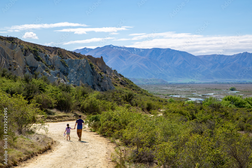 A father and daughter returning along a track to the Clay Cliffs overlooking the river valley at Omarama, New Zealand