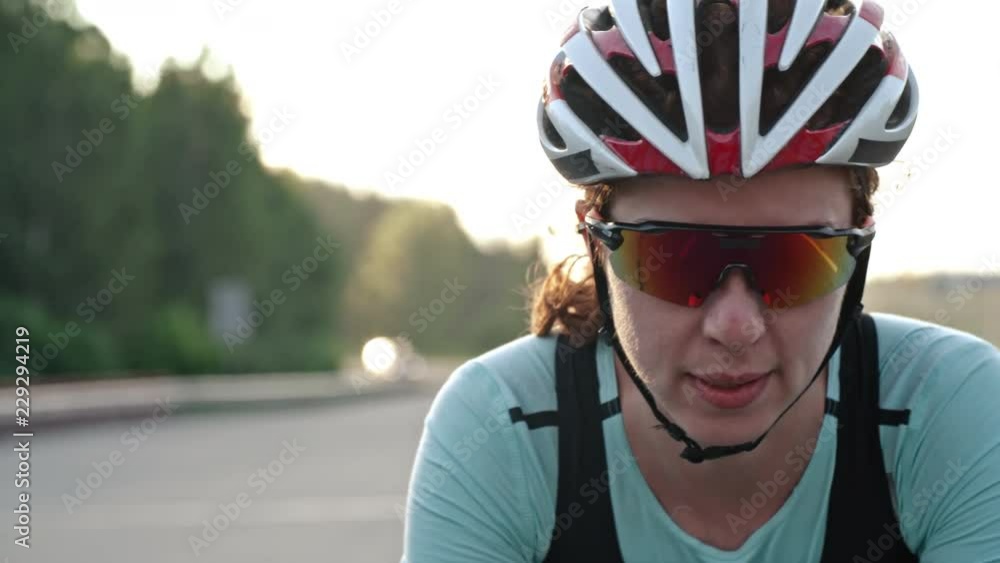 Dolly with tilt down of concentrated professional female cyclist in protective sunglasses and helmet riding bicycle along freeway Dolly with tilt down of concentrated professional female cyclist in protective sunglasses and helmet riding bicycle along freeway