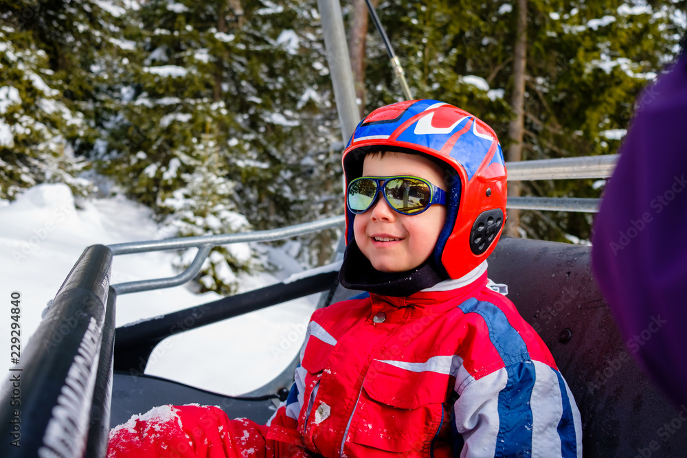 Happy Child with Helmet Sitting in a Chairlift for Ski Happy Child with Helmet Sitting in a Chairlift for Ski