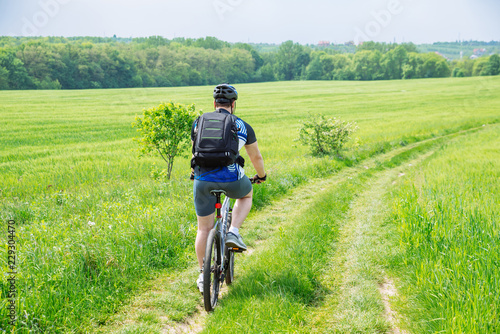 man riding bicycle by trail in green barley field. copy space