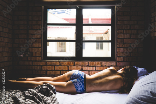 A young woman laying uncovered on a bed in only underwear