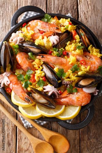 Paella seafood with king prawns, mussels, fish, and baby octopus served in a pan on a wooden table. Vertical top view