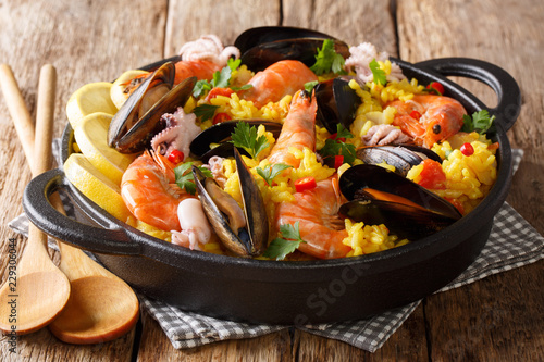 Homemade freshly prepared paella with king prawns, mussels, fish, and baby octopus served in a pan on a wooden table. horizontal