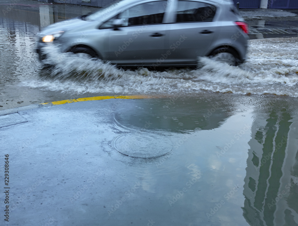 Blurred car driving along flooded street splashing water Blurred car driving along flooded street splashing water