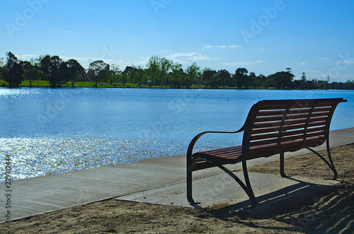 Empty bench facing lake with blue sky and blue water