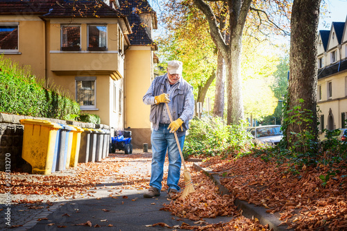 Senior sweeping autumn leaves.