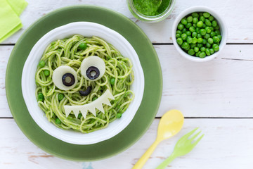 Fun food for kids - cute smiling face of green spaghetti monster served in a white bowl with eyes made of cheese and olives. Healthy vegetarian eating for children