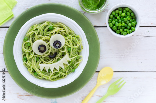 Fun food for kids - cute smiling face of green spaghetti monster served in a white bowl with eyes made of cheese and olives. Healthy vegetarian eating for children photo