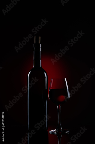 A bottle of red wine with a half full wine glass using stripbox for rim light effect