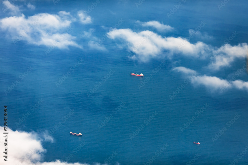 Aerial view through a veil of clouds on three cargoships floating in ocean waters. Aerial view through a veil of clouds on three cargoships floating in ocean waters.