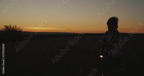 A cute boy playing with a flashlight at sunset through the grass. photo