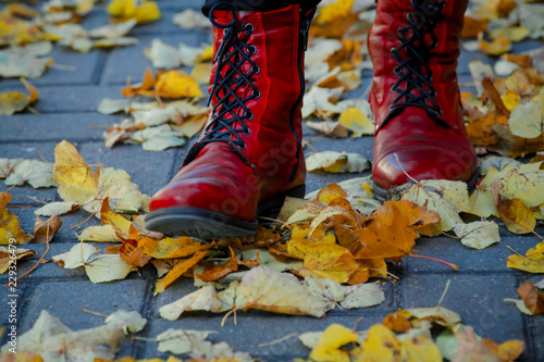 Girl in red boots standing on the sidewalk with fallen leaves.