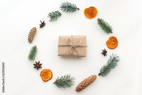 Composition with christmas gift in craft paper, dried orange and mandarin, anise stars, cinnamon, pine cones, fir branches on white background. Flat lay, top view