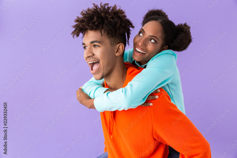 Obraz premium Photo of pleased african american man piggybacking his teenage sister, isolated over violet background