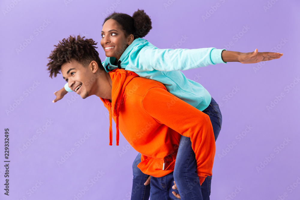Obraz premium Photo of beautiful african american guy piggybacking his girlfriend, isolated over violet background
