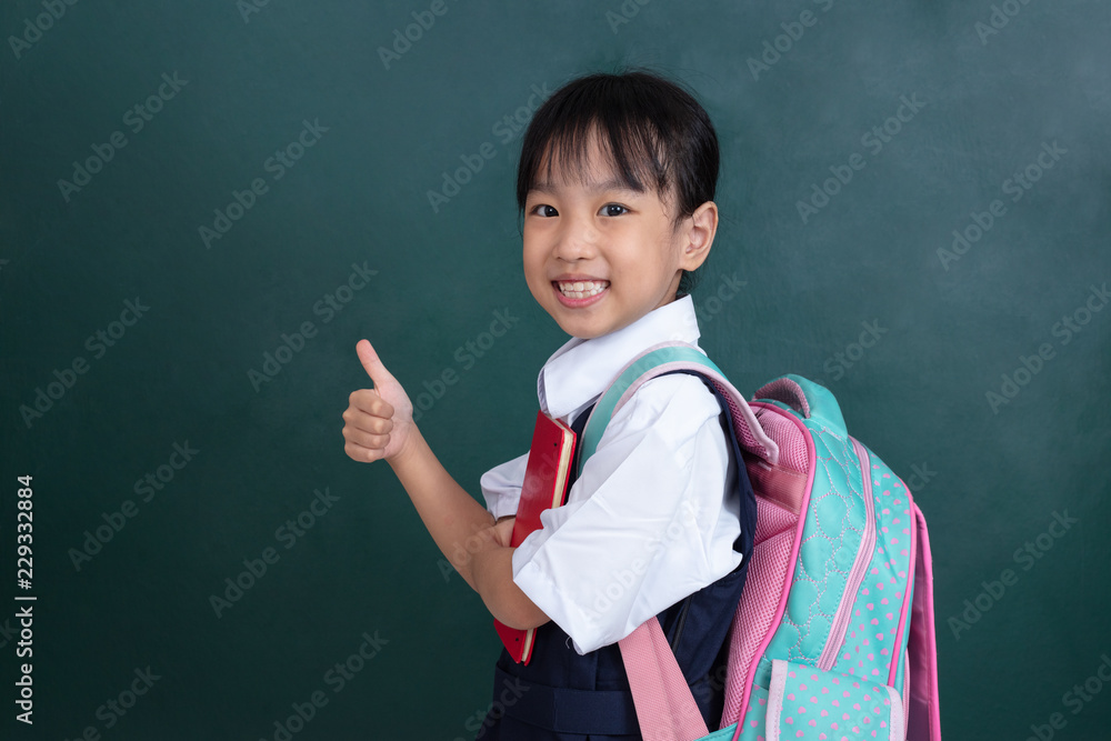 Φωτογραφία Asian Chinese little Girl in uniform showing thumbs up against green blackboard