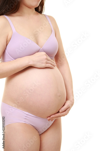 大きくなったお腹を労わる薄紫色の下着を着た臨月の妊婦