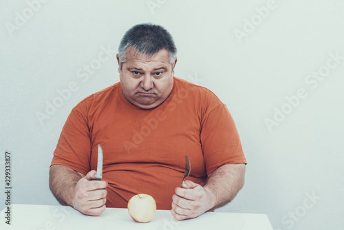 Fat Man with Knife and Fork with Apple on Table. photo