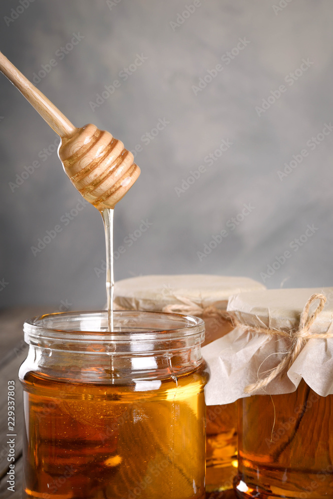 Pouring aromatic honey into jar, closeup. Honey in glass jars and honeycombs wax on wooden background. Wooden stick , instruments Pouring aromatic honey into jar, closeup. Honey in glass jars and honeycombs wax on wooden background. Wooden stick , instruments