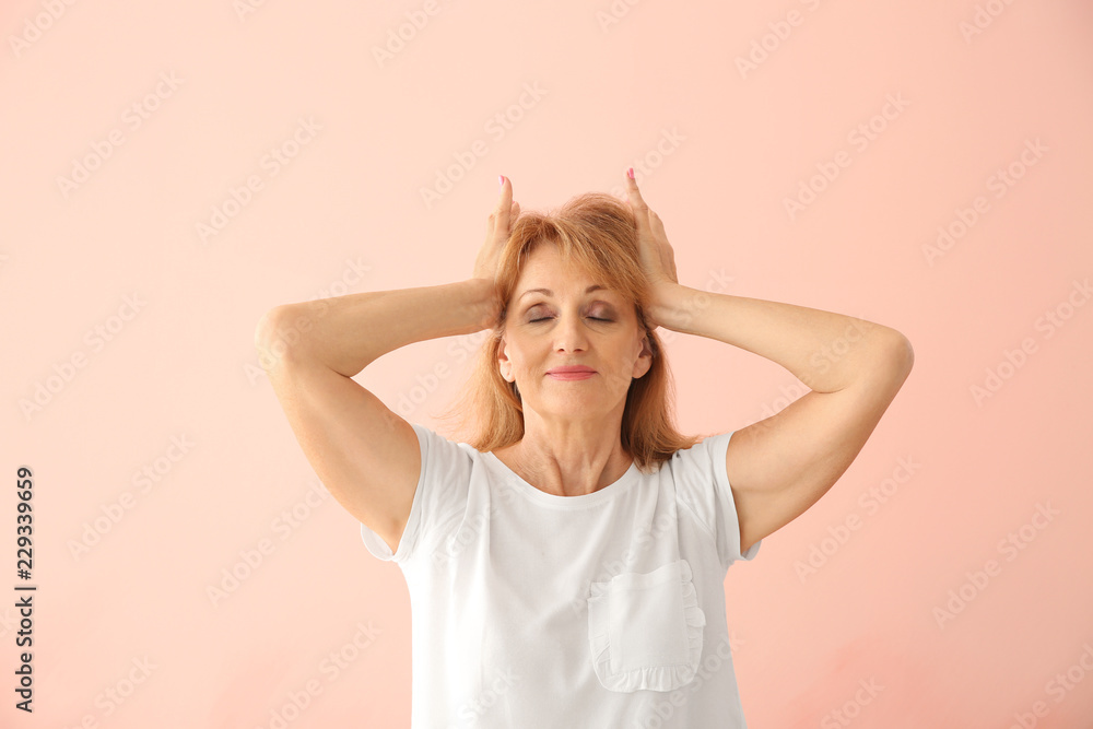 Portrait of mature woman pressing hands to her head on color background Portrait of mature woman pressing hands to her head on color background