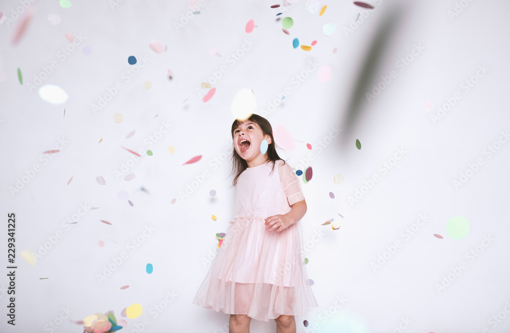 Happy beautiful little girl wearing pink dress with princess crown enjoying colorful confetti surprise falling down, posing on white studio wall. Pretty girl celebrating her birthday party, having fun Happy beautiful little girl wearing pink dress with princess crown enjoying colorful confetti surprise falling down, posing on white studio wall. Pretty girl celebrating her birthday party, having fun