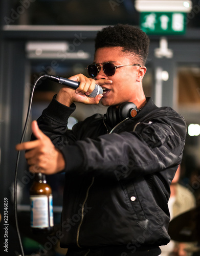 Black rapper performing with microphone, holding bottle. Headphones around neck
