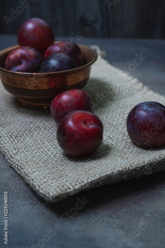 Plums with a bowl on a rural wooden table. Moody and dark style concept. (Prunus domestica)
