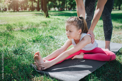 A picture of small girl stratching. Adud woman is helping her to do that right. Girl is keeping her left foot close to right leg. Yoga and Pilates Concept. photo