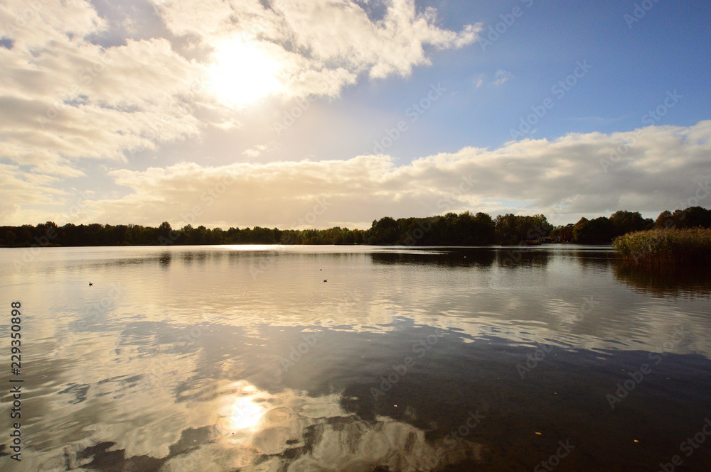 Fototapeta premium Pochmurny dzień nad jeziorem i słońce za chmurami.