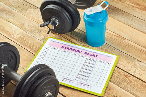 Healthy lifestyle concept. Mock up on workout and fitness dieting diary. Exercise diary sheet, blue shaker and dumbbells on a rustic wooden background