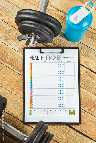 Healthy lifestyle concept. Mock up on workout and fitness dieting diary. Health tracker sheet, blue shaker and dumbbells on a wooden background.