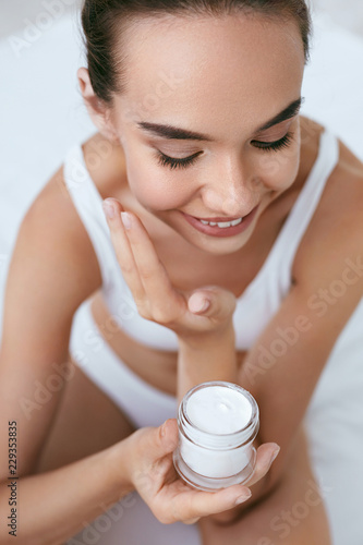Fototapeta Naklejka Na Ścianę i Meble -  Beauty Skin Care. Beautiful Woman Applying Cream On Face Skin