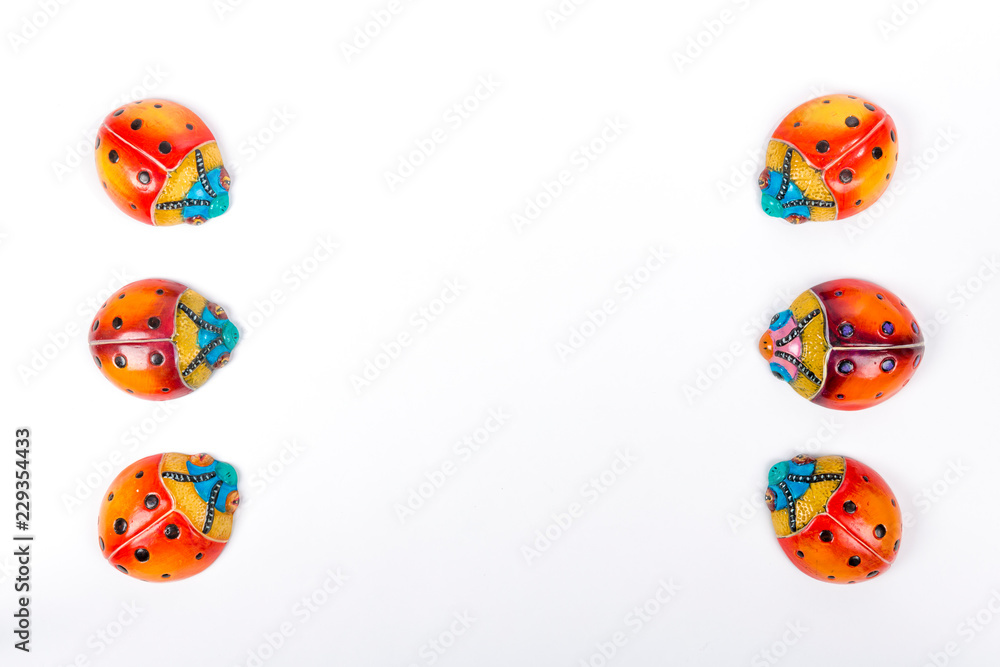Flat lay of two small line formed by three of ceramic ladybugs on a white studio background, red, orange, yellow, blue and black colors. Space for text