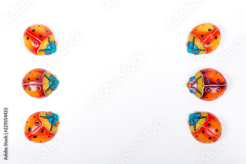 Flat lay of two small line formed by three of ceramic ladybugs on a white studio background, red, orange, yellow, blue and black colors. Space for text