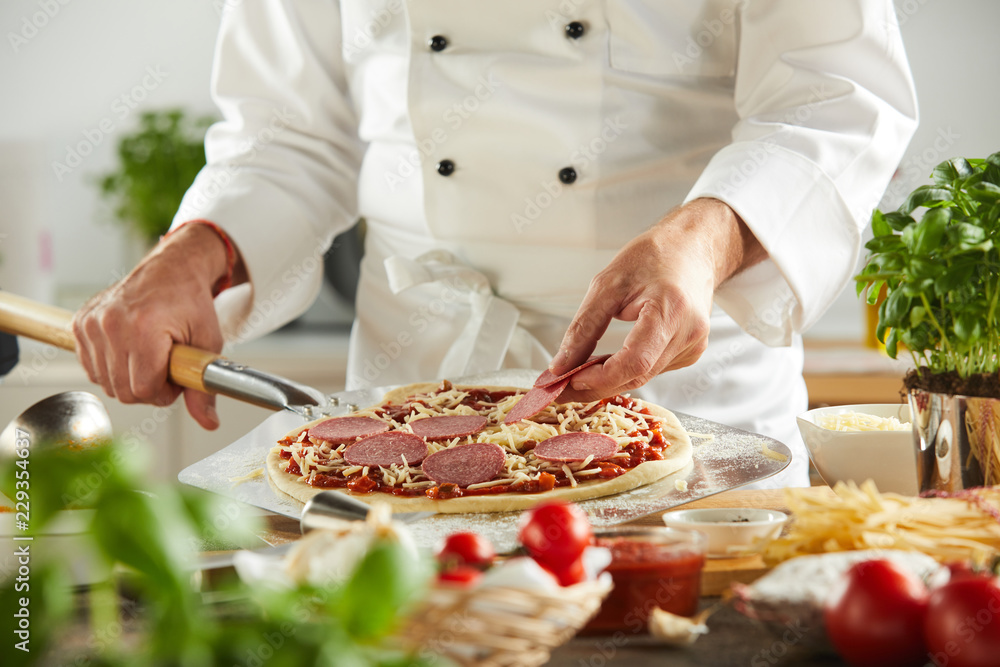 Chef carefully placing pepperoni slices on pizza