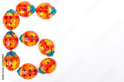 Flat lay with the number 6 formed by a group of ceramic ladybugs with red, orange, yellow, blue and black colors on a white background with space for text