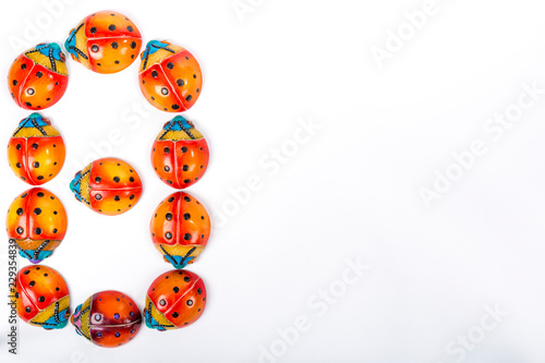 Flat lay with the number 8 formed by a group of ceramic ladybugs with red, orange, yellow, blue and black colors on a white background with space for text. March 8, International Women's Day