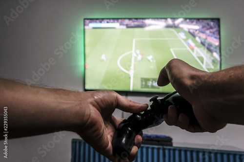 Man hold gamepad in hands in front of  tv screen with Pro Evolution Soccer. One gamer. Widescreen tv hanging on the wall photo