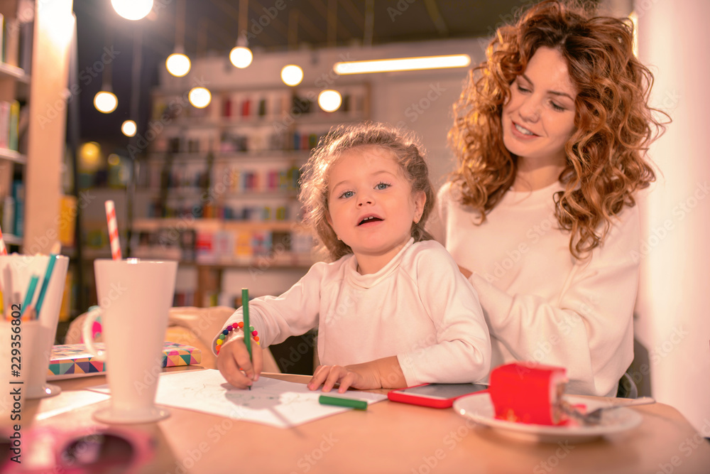 New hairstyle. Attentive baby girl leaning arms on table while posing on camera New hairstyle. Attentive baby girl leaning arms on table while posing on camera