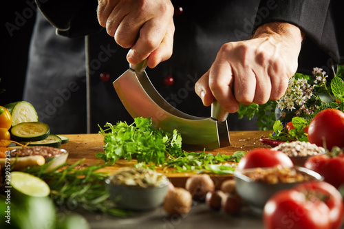 Chef chopping fresh herbs with a mezzaluna knife photo