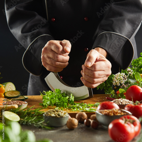 Chef using a mezzaluna knife to chop herbs photo