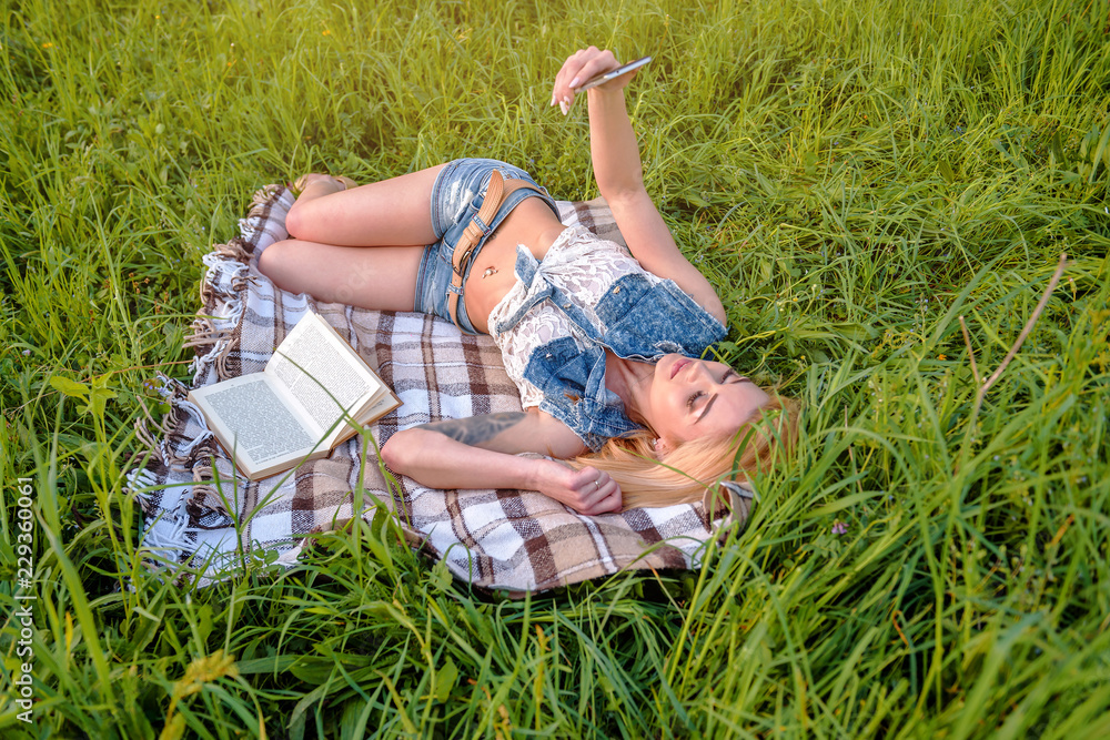 young blonde girl resting with book and smartphone in the park young blonde girl resting with book and smartphone in the park