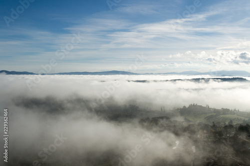 A view from an high tower in the little town of San Gimignano, tuscany italy. A sea made of fog until the horizon with light blue mountains in the background and a little town emerging from the mist  © eugpng