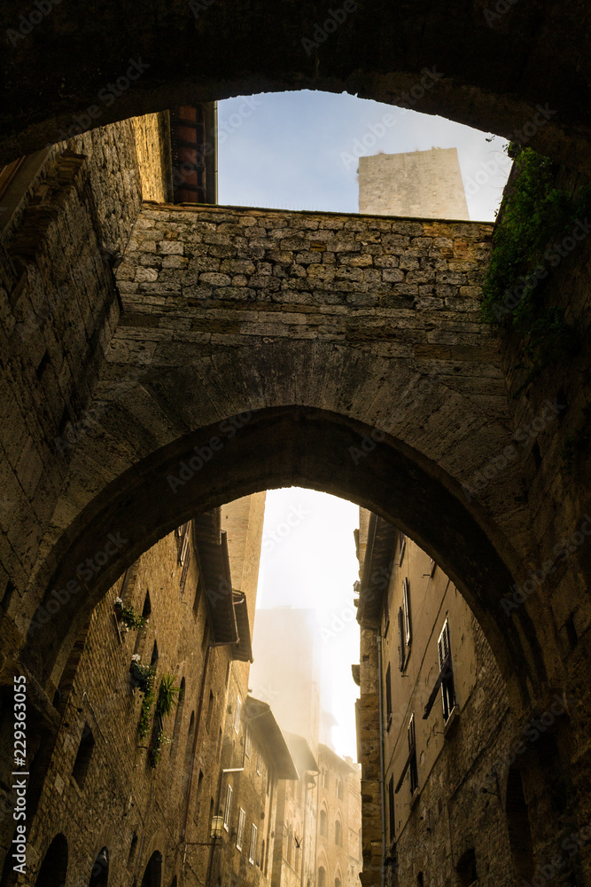 Walking through and under arcades in a narrow alley in San Gimignano, a little perched town with many medieval towers.