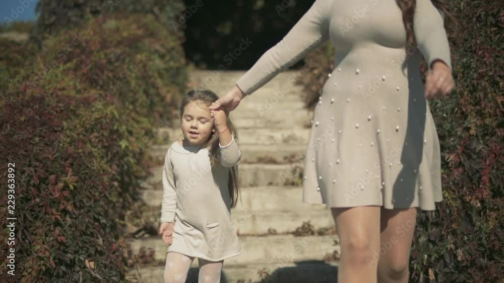 Gorgeous mom and beautiful daughter go down the stairs in the park. Slow motion Gorgeous mom and beautiful daughter go down the stairs in the park. Slow motion