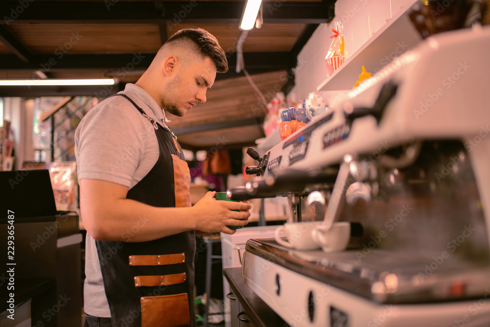 Conscious worker. Serious brunette man bowing head while warming up milk for latte Conscious worker. Serious brunette man bowing head while warming up milk for latte